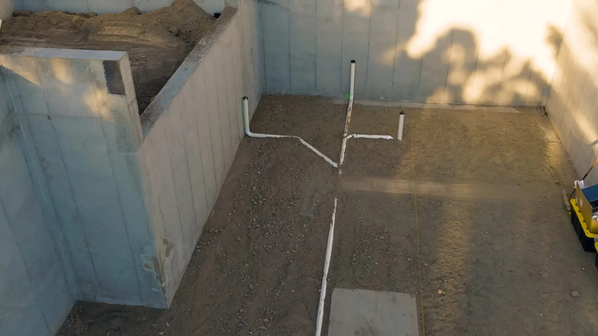 Bare concrete slab inside a tiled room with white PVC pipes standing up from the floor