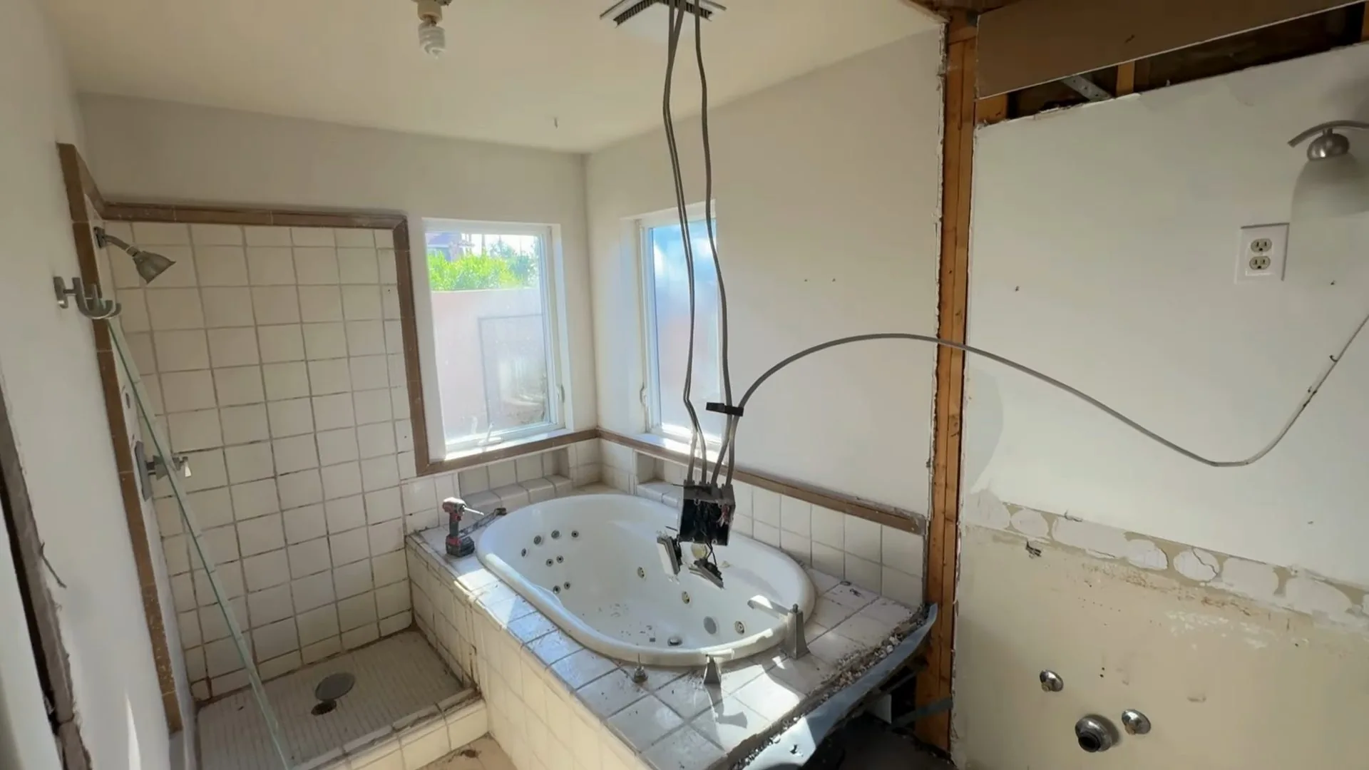 Bathroom with a jetted tub, opened wall cavities, bare studs and a cable hanging from the ceiling