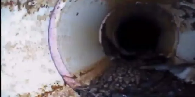 Camera view down the inside of a white pipe with a joint ring and scattered debris at the bottom