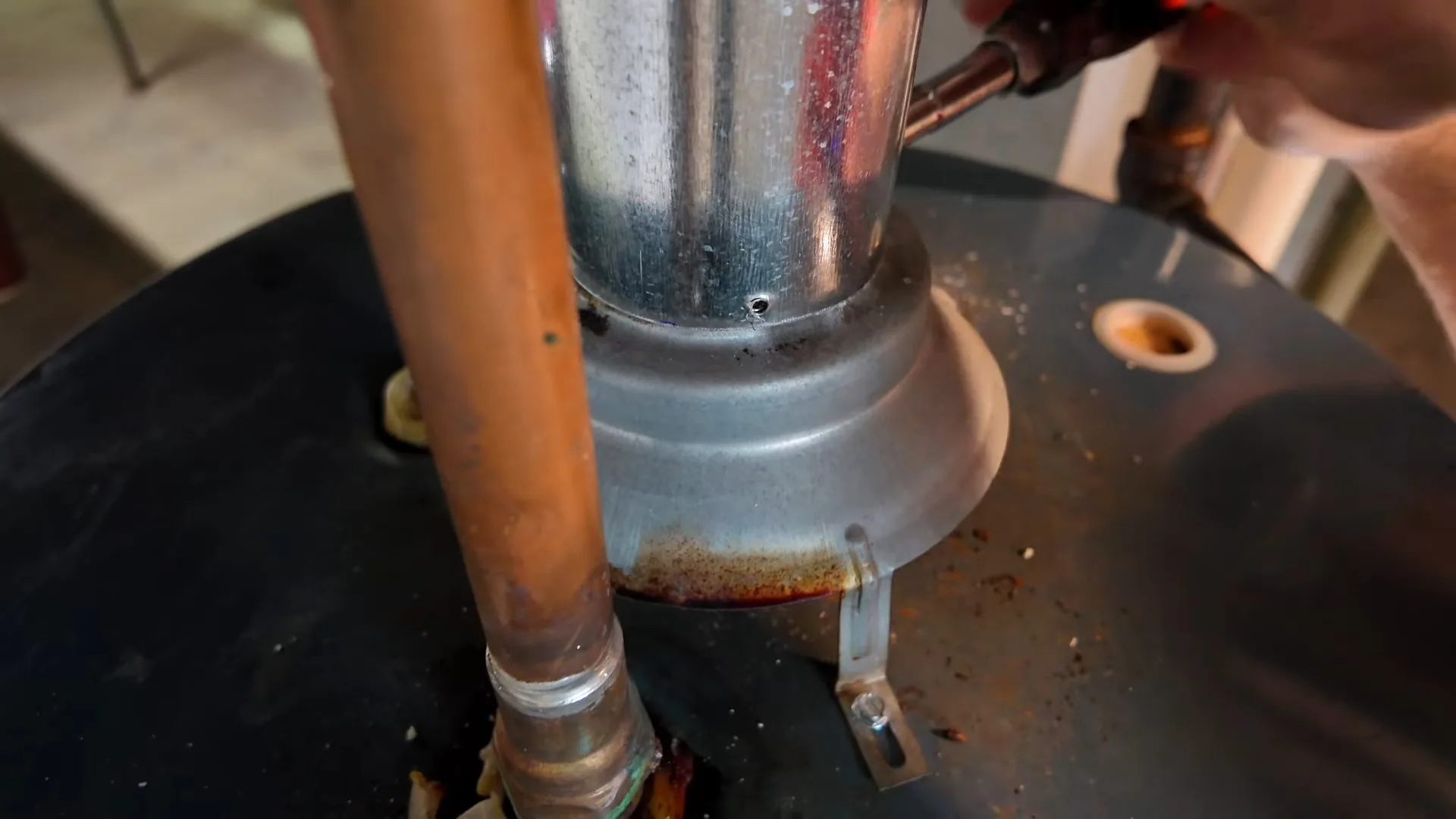Copper pipe and a steel vent collar on top of a black tank water heater with a hand working beside the fitting