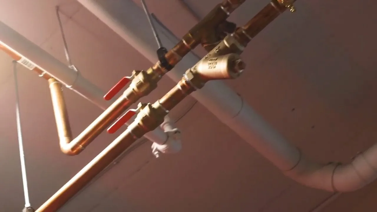 Copper supply pipes running along a ceiling with two red-handled ball valves