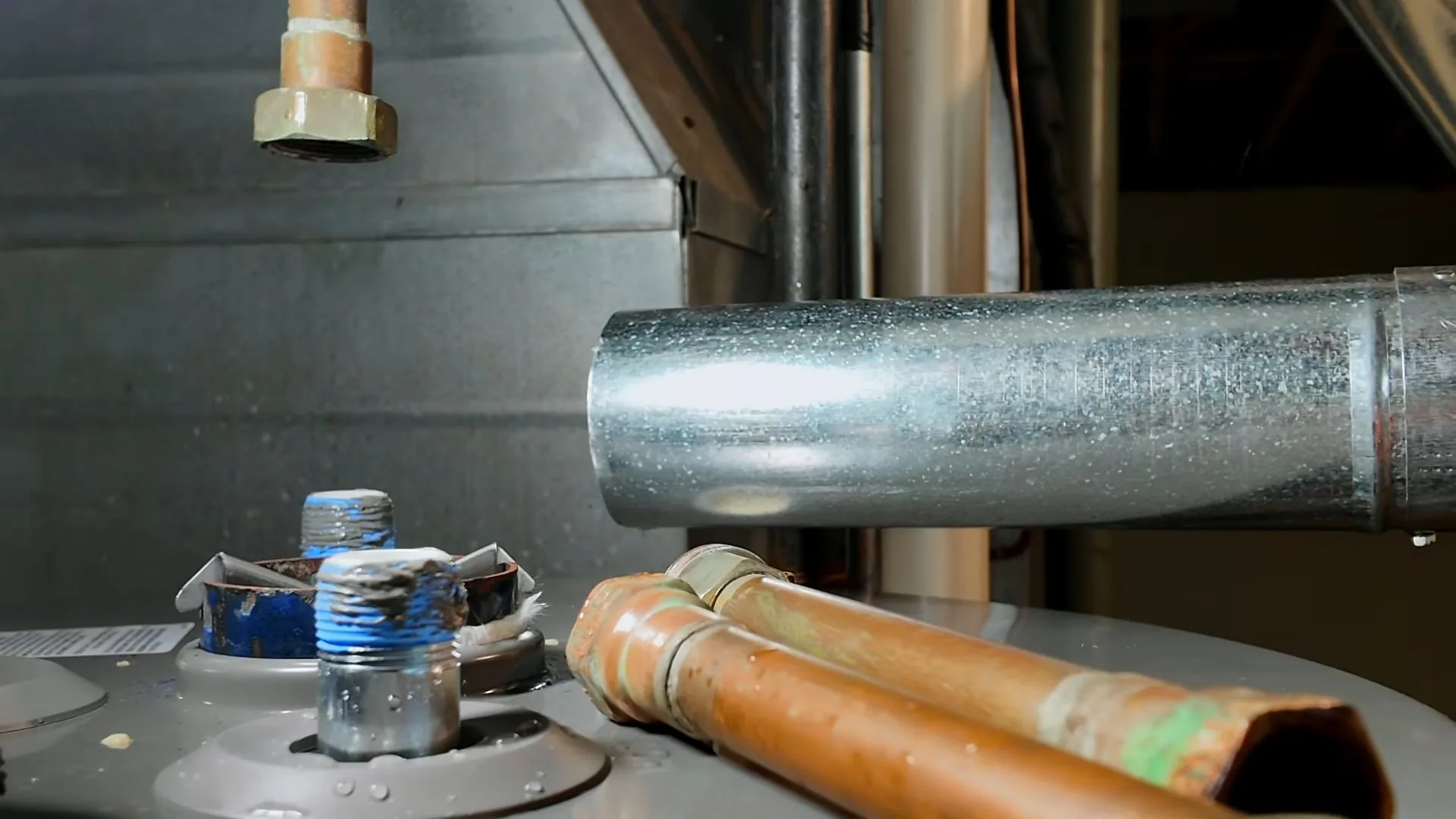 Top of a tank water heater with two copper supply pipes, a steel vent pipe and a blue-taped threaded fitting