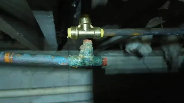 Copper pipe with blue-green corrosion and a brass tee and valve in a dark crawlspace under floor joists