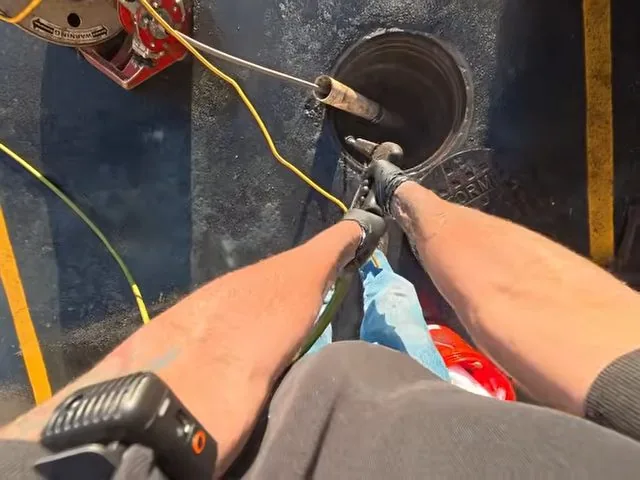 View from above of hands feeding a yellow drain cable into a round cleanout opening in a floor