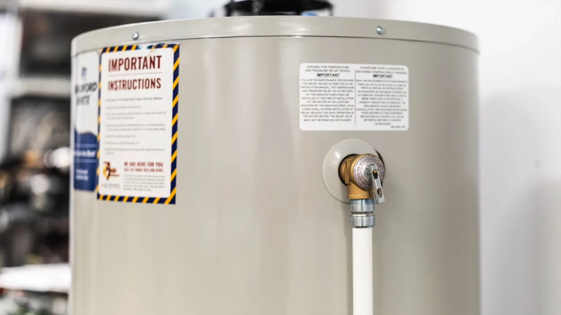 Close view of a cream-colored electric water heater with an instruction label and a brass relief valve at the side
