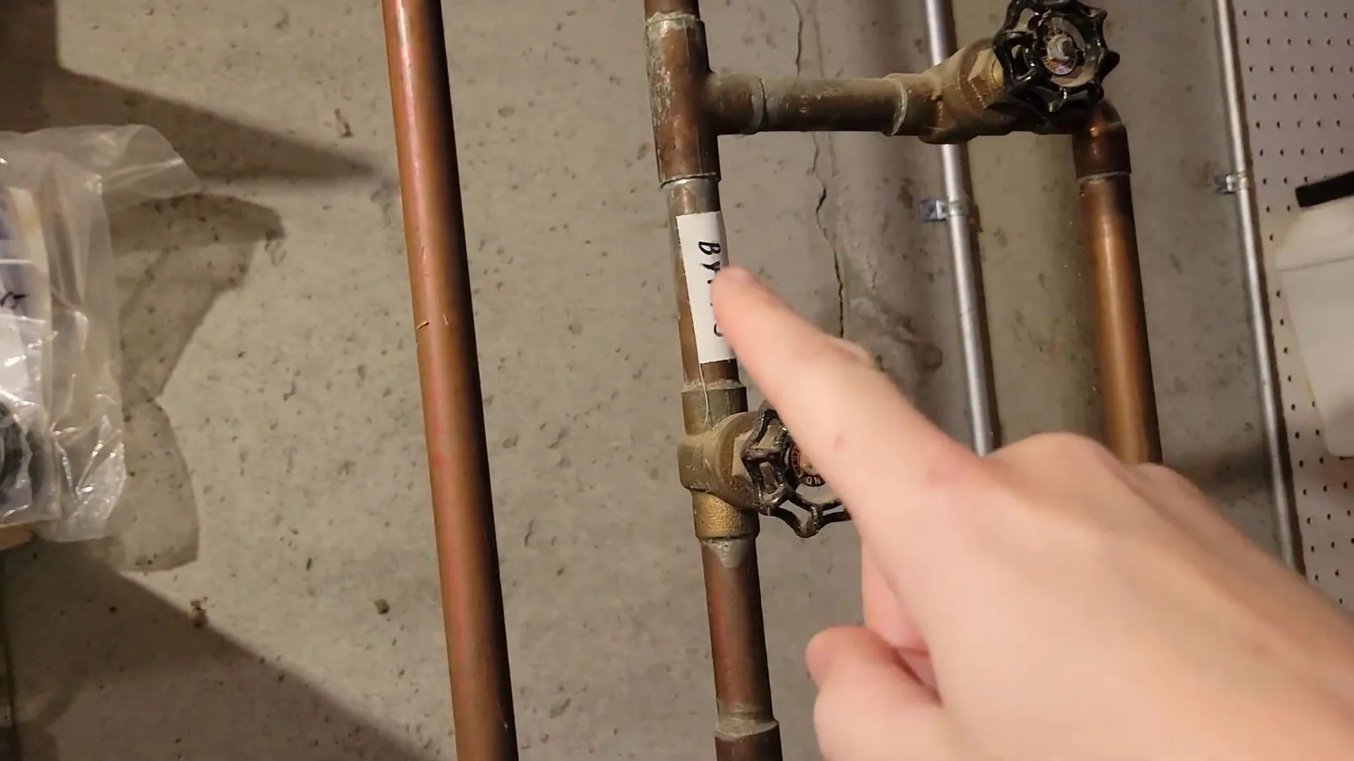 Finger pointing at a black-handled brass shutoff valve on a vertical copper supply line