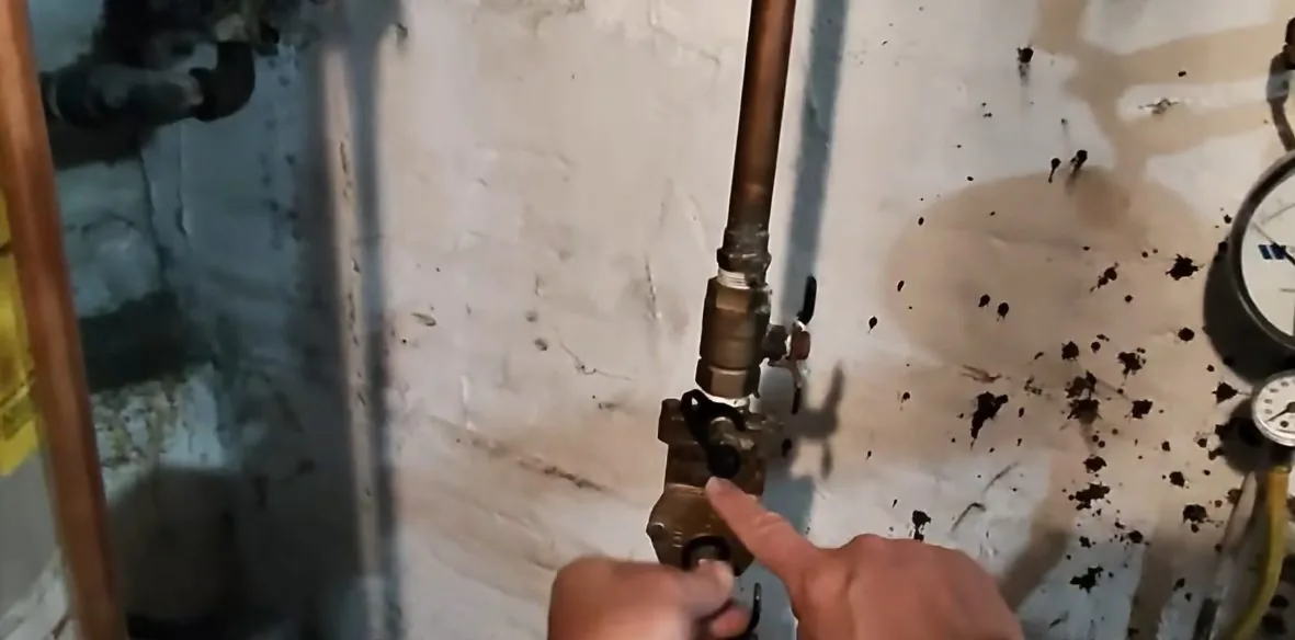 Finger pointing at a brass valve on a copper pipe beside a water meter on a stained wall