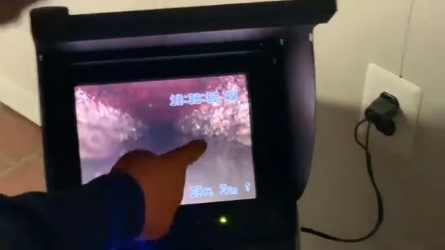Hand pointing at a handheld camera monitor showing the pink interior of a pipe