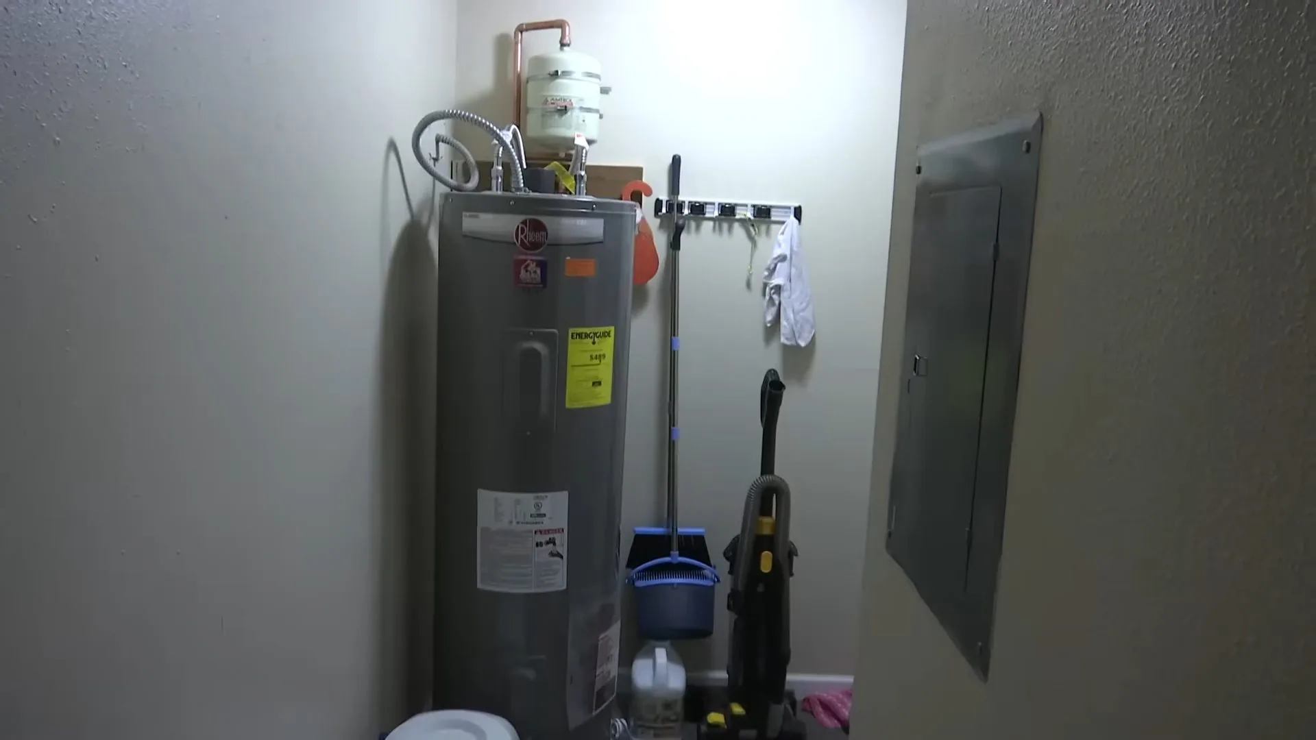Gas tank water heater standing in a utility room beside an electrical panel and a mop bucket