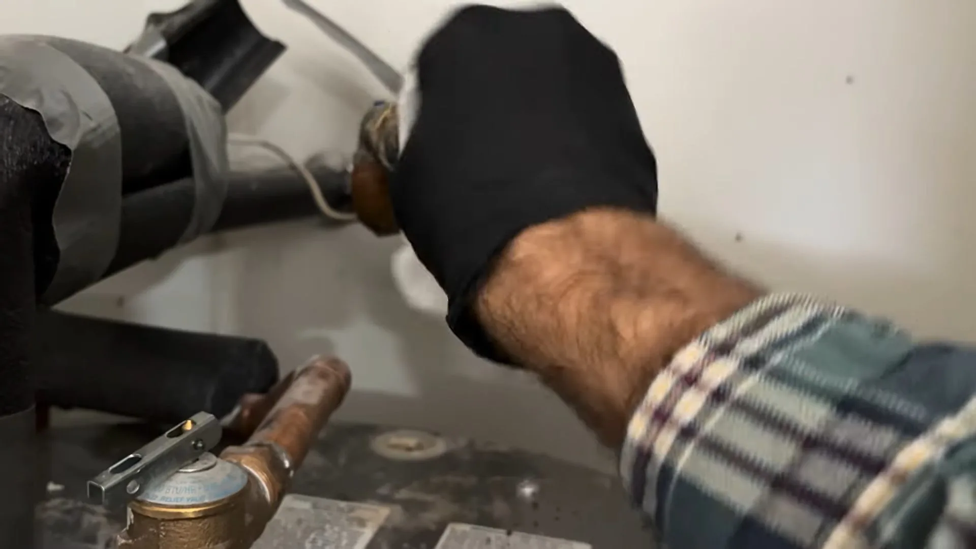 Hand in a black glove resting on an insulated pipe beside a brass valve