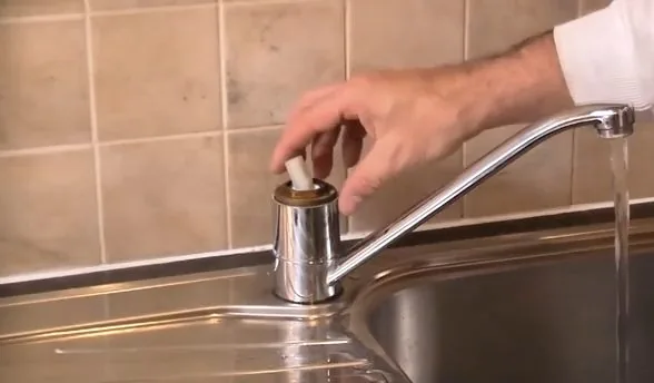 Hand fitting a cap onto the handle of a chrome kitchen faucet beside a tiled backsplash