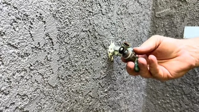 Hand on the valve handle of a brass hose bib mounted on a textured stucco wall