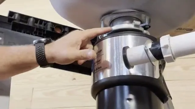 Hand resting on the side of a stainless garbage disposal mounted under a sink, with white drain pipe attached