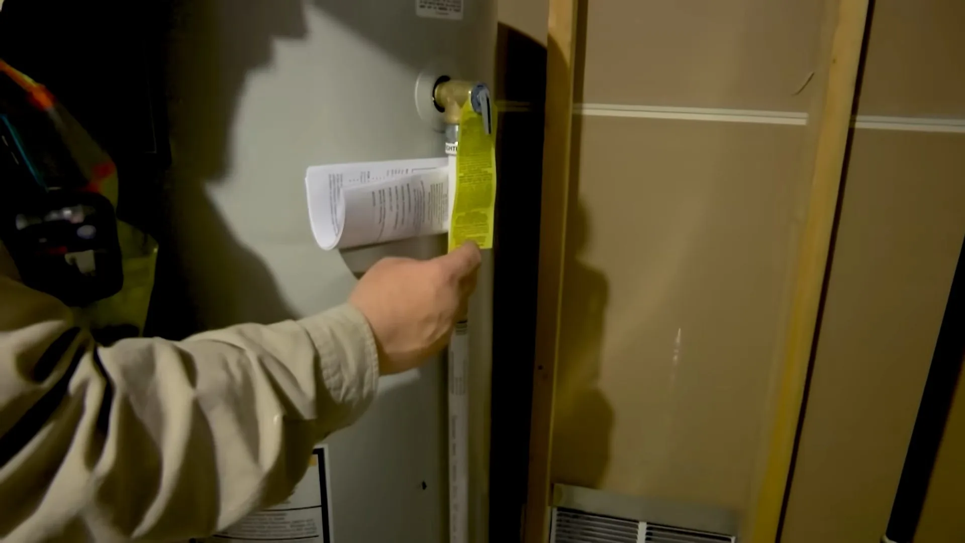 Hand in a gray sleeve pressing a paper label onto the wall beside a water heater closet