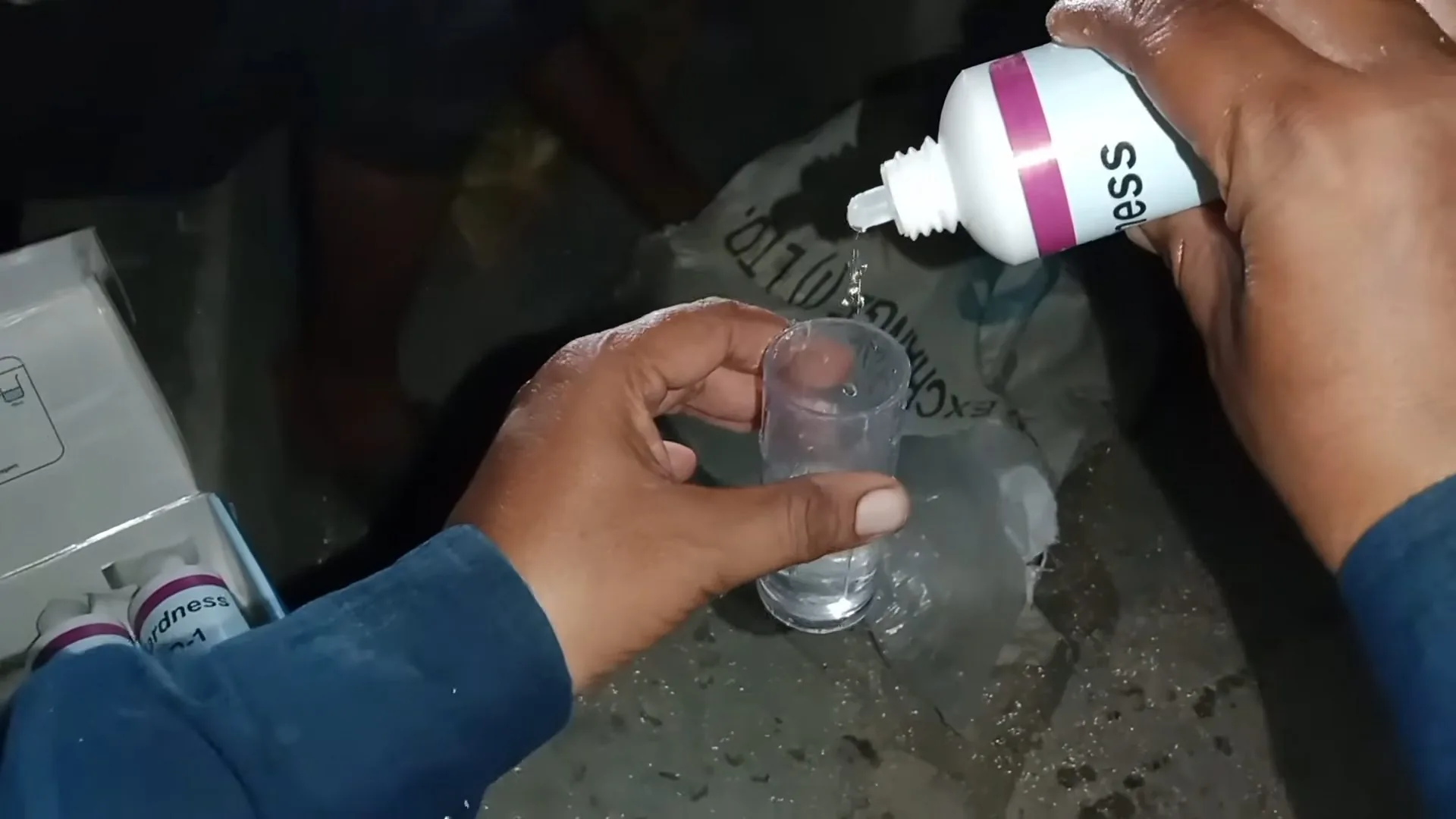 Hands holding a small glass of water while a reagent bottle drips into it