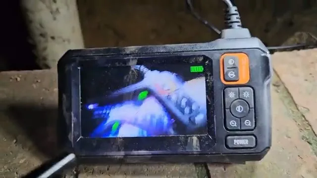 Handheld inspection camera screen showing blurred blue and green shapes inside a pipe, resting on a wooden beam