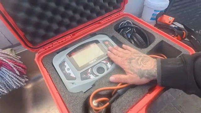 Open red hard case holding a handheld inspection device, with a tattooed hand resting on it