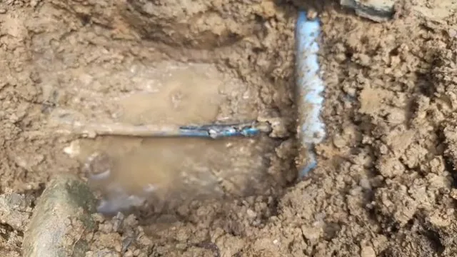 Muddy excavation with a light blue pipe and a pool of brown water around a joint