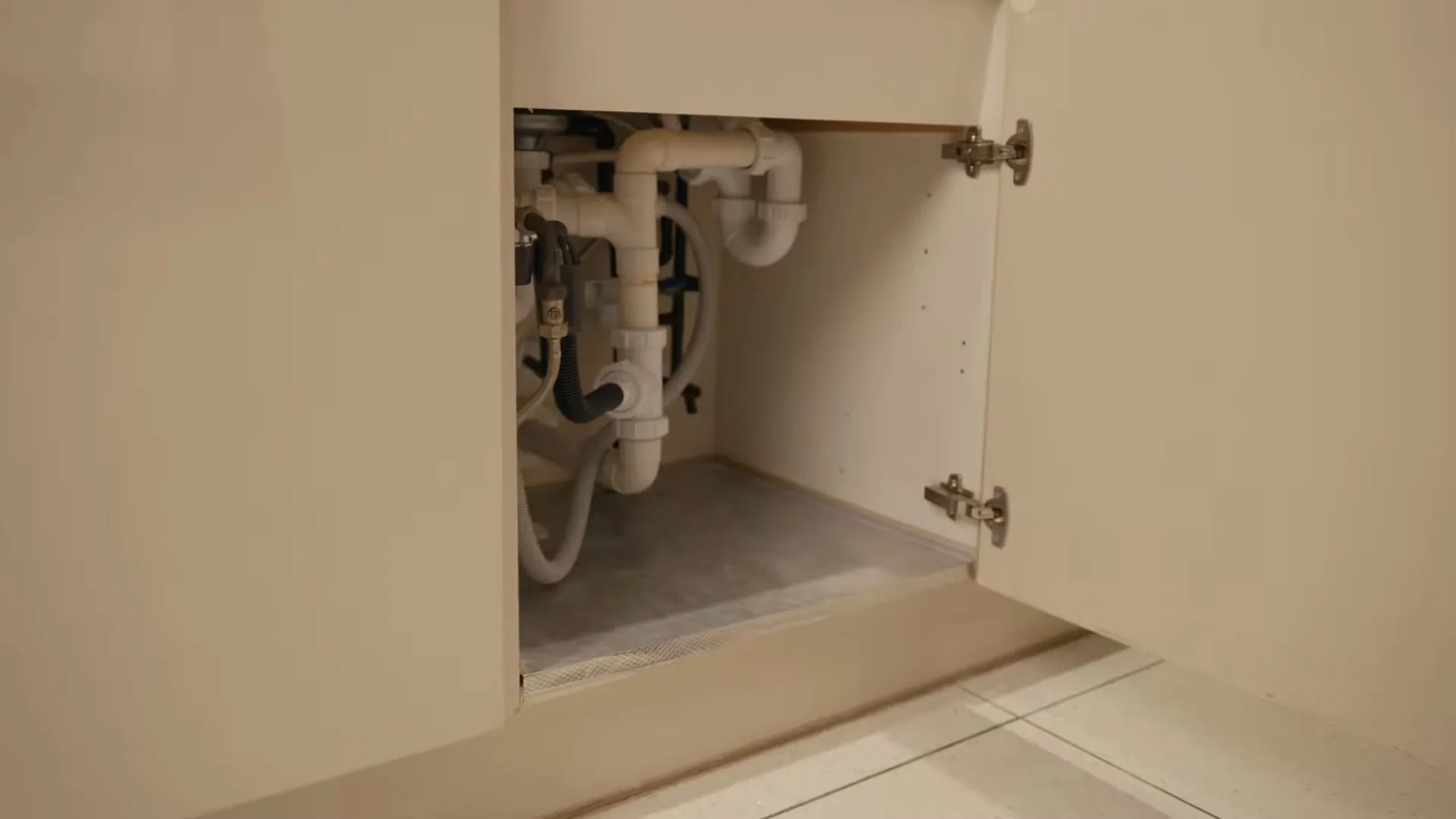 Open cabinet under a sink showing a white P-trap and drain pipes against the back wall