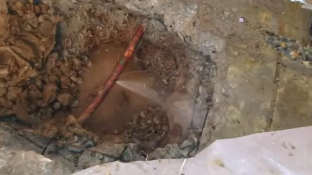 Hole cut into a concrete floor with a copper pipe spraying water inside a wet excavation