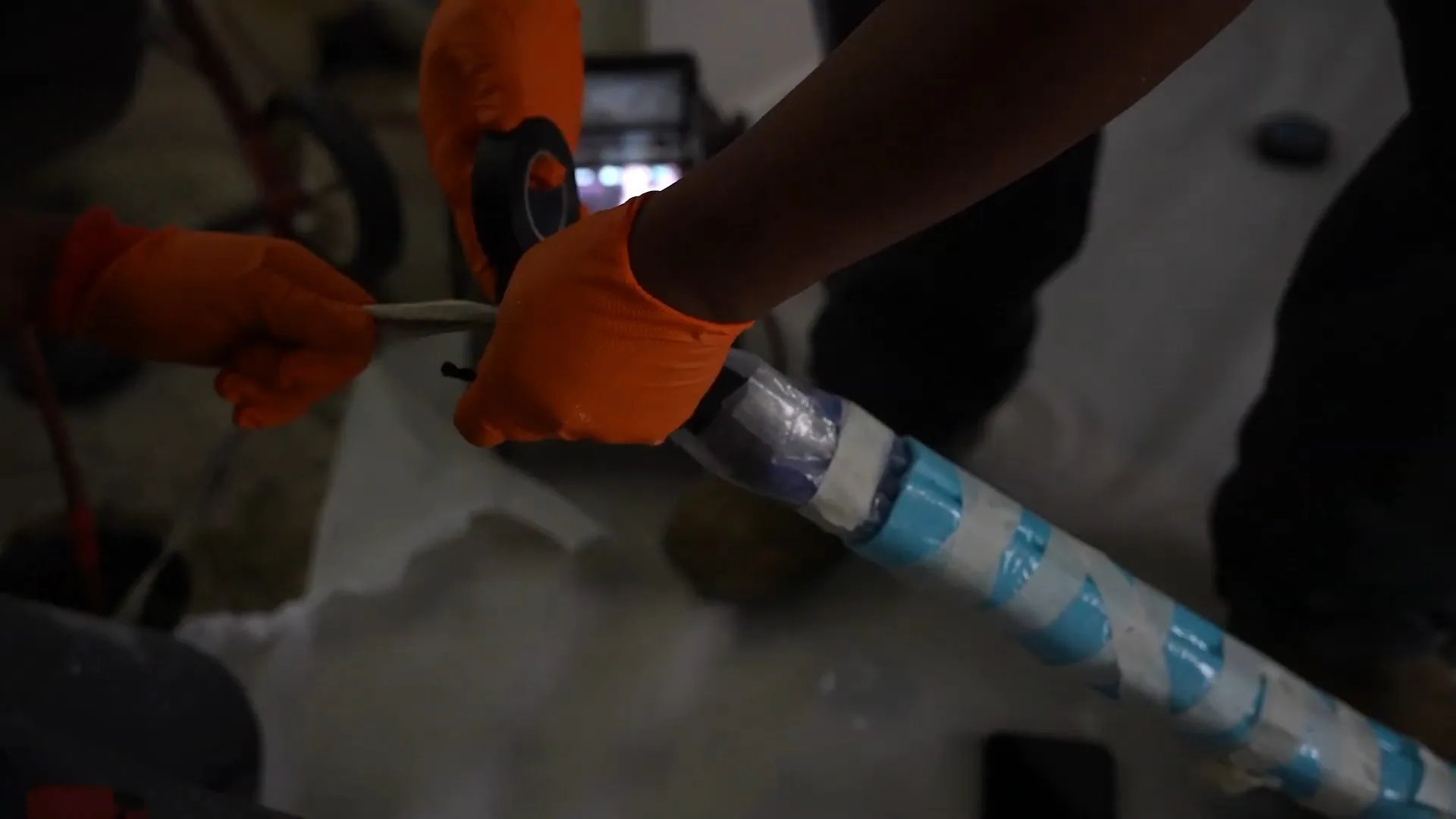 Hands in orange gloves handling a pipe liner wrapped in blue spiral tape
