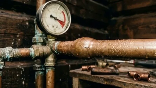 Round pressure gauge on copper and brass pipes with water beads on the pipe, in a room with dark wood walls