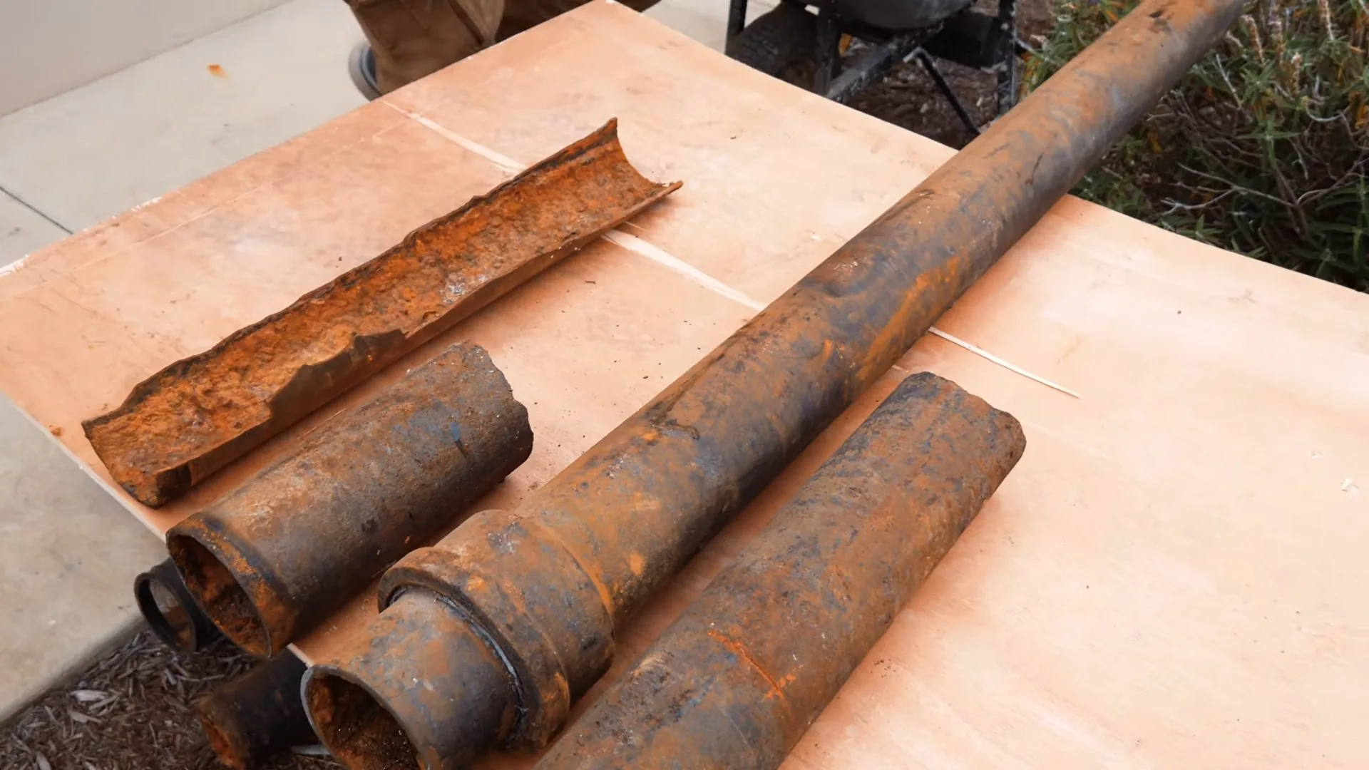 Four rusted lengths of old iron pipe on a plywood sheet, one split open along its length
