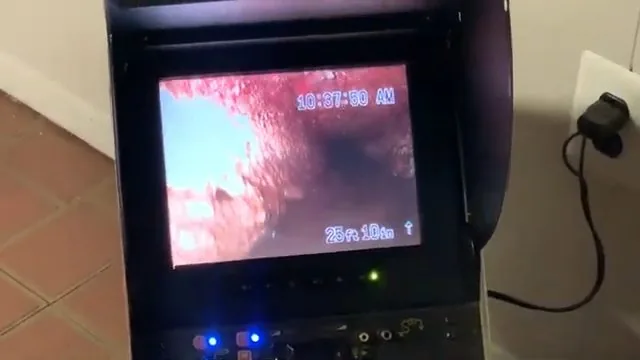 Camera monitor on a stand showing the pink interior of a sewer pipe with a timestamp