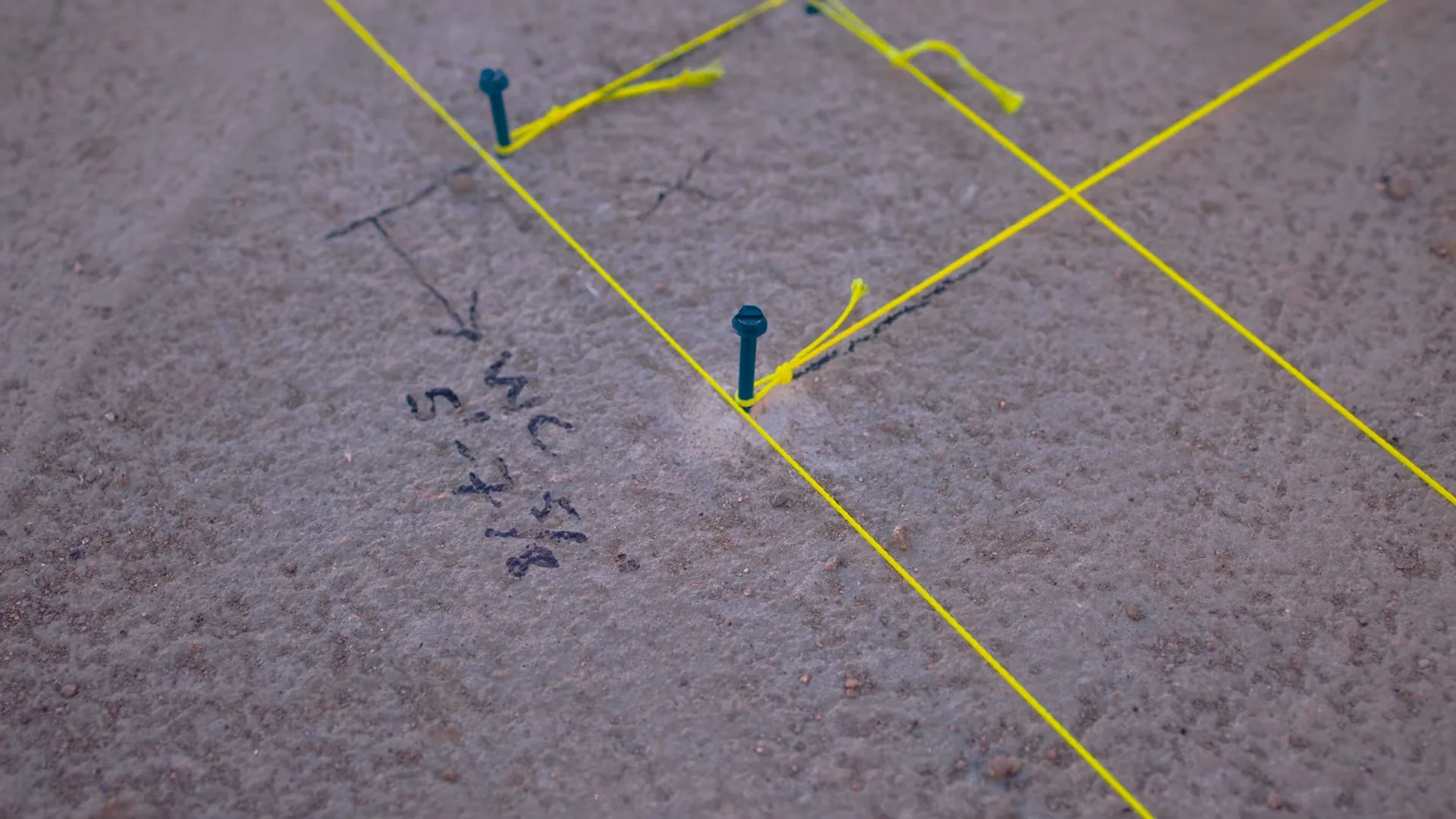 Concrete slab floor with yellow chalk lines, small blue flags and handwritten notes marking a pipe route