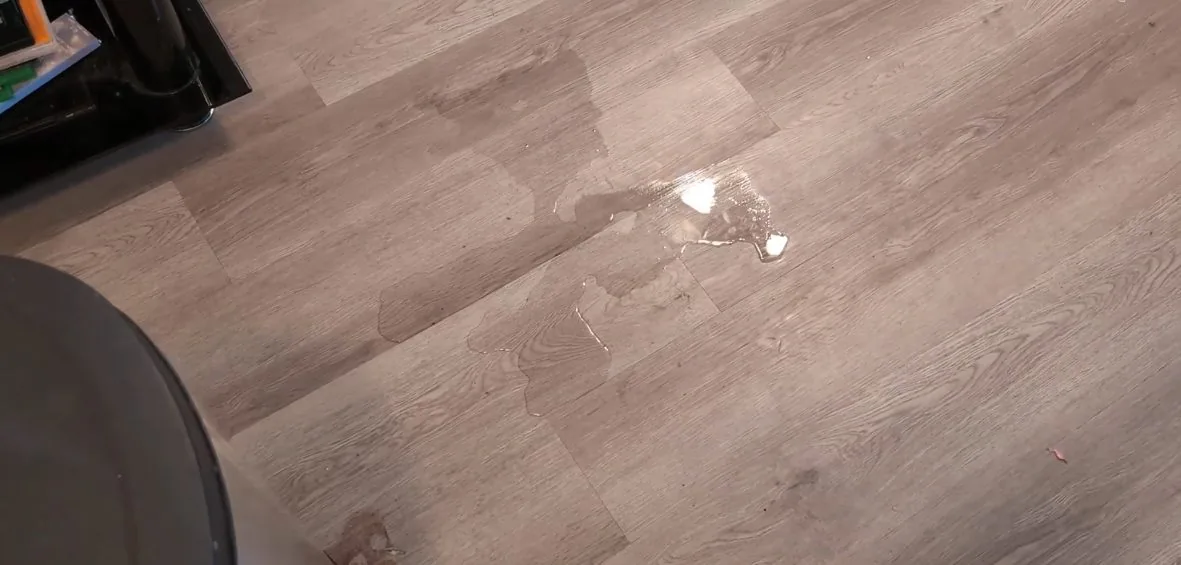Drop of water on a wood-look vinyl plank floor beside the edge of a chair