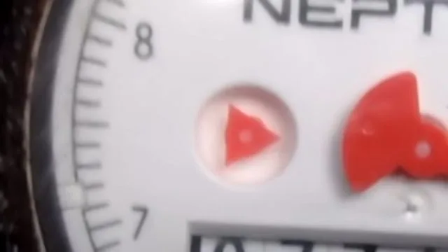 Close view of a water meter dial with a red triangle flow indicator beside the numbered scale