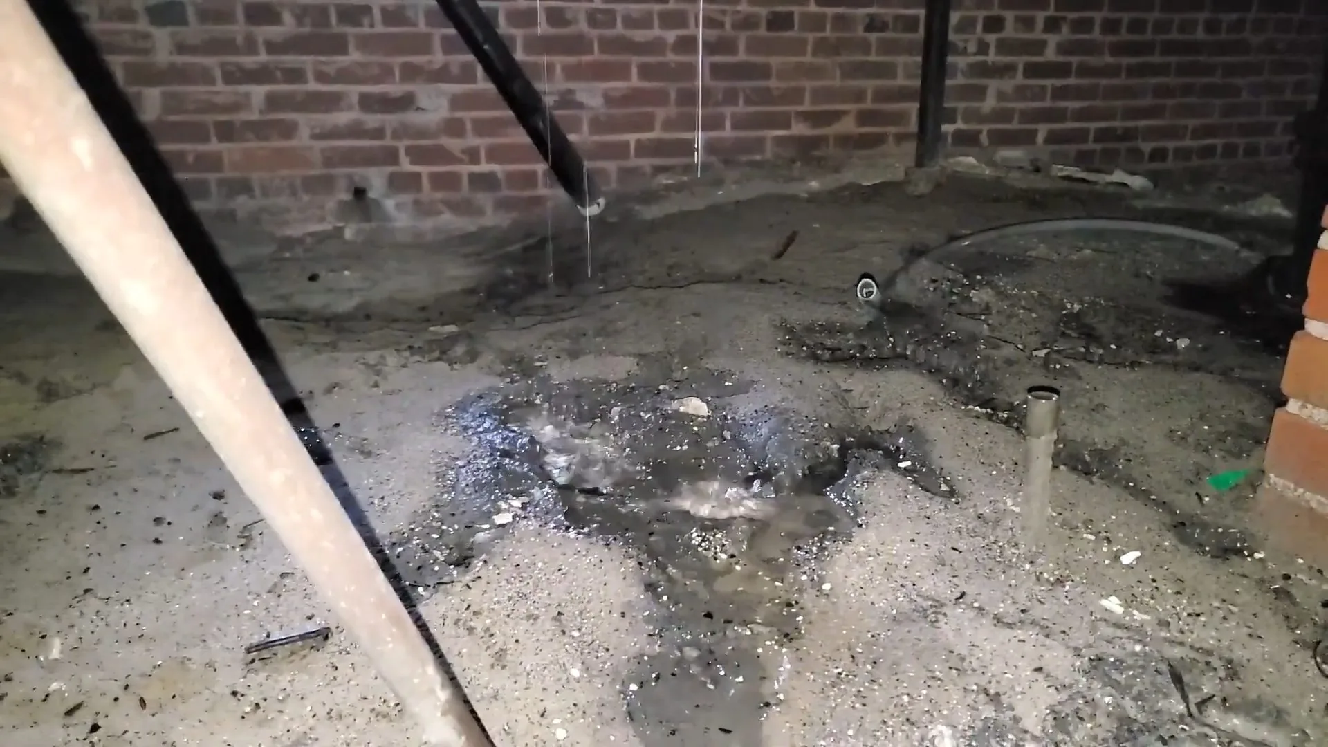 Dark wet soil under a crawlspace floor around a pipe stub beside a brick pier