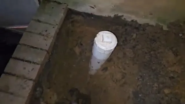 White PVC pipe standing up in a dirt pit beside a brick edge