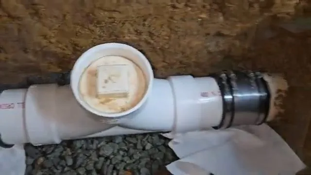 White PVC cleanout tee with a screw cap set in a gravel-lined pit