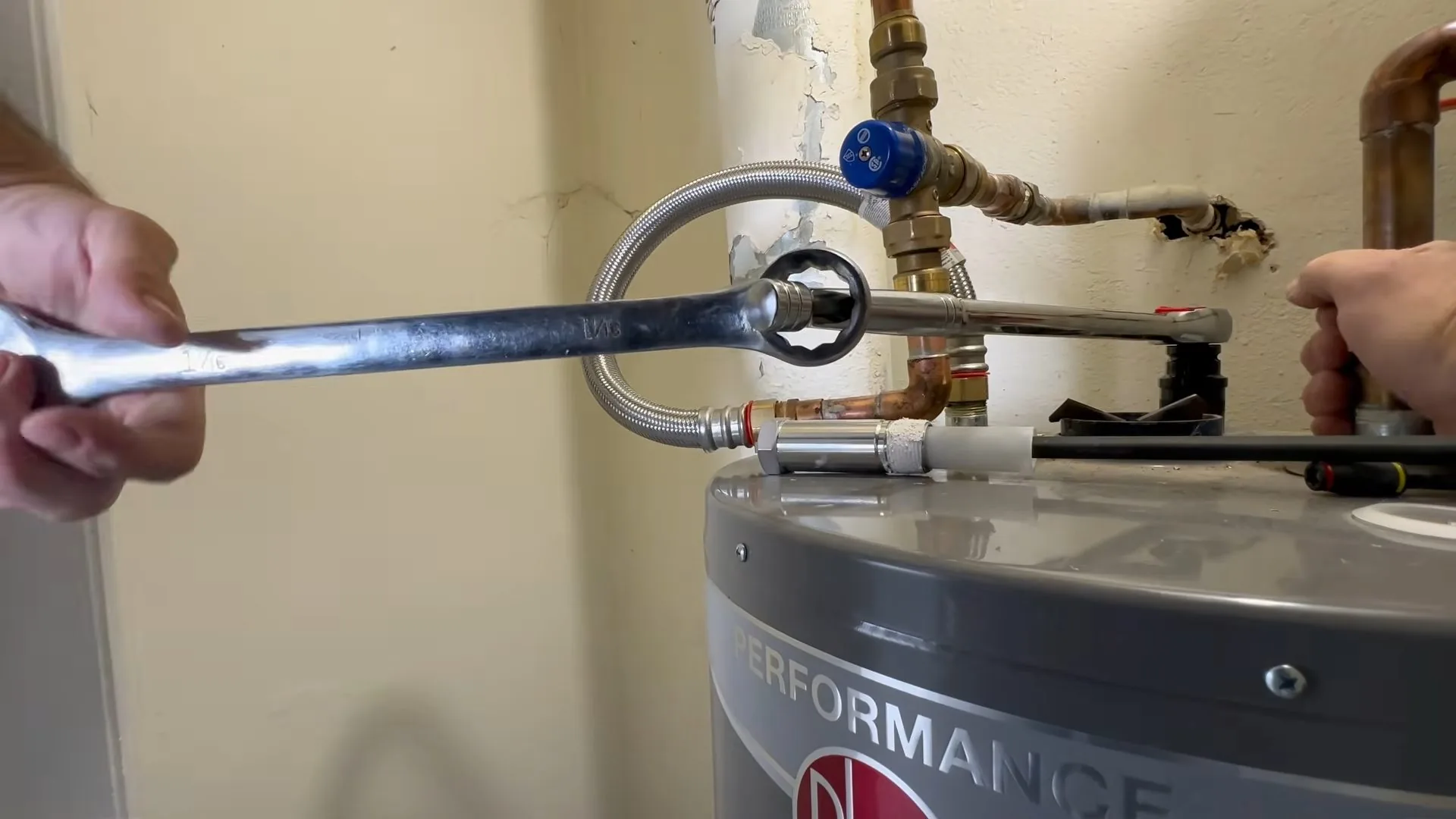 Open-end wrench on a stainless flexible connector at the top of a gray water heater